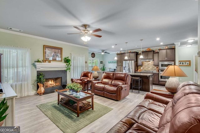 living area featuring a lit fireplace, light wood-type flooring, a ceiling fan, and visible vents