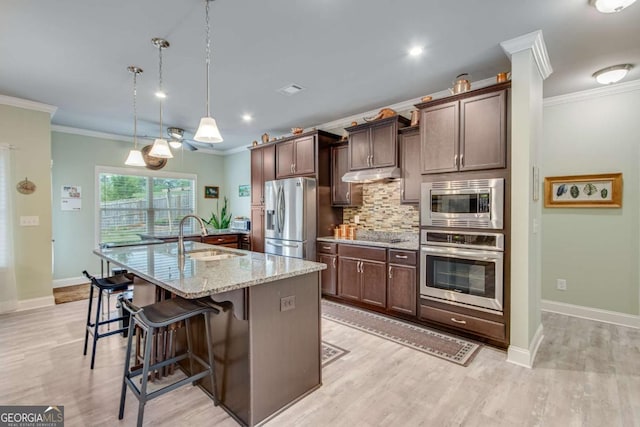 kitchen featuring a breakfast bar area, a sink, crown molding, a center island with sink, and stainless steel appliances
