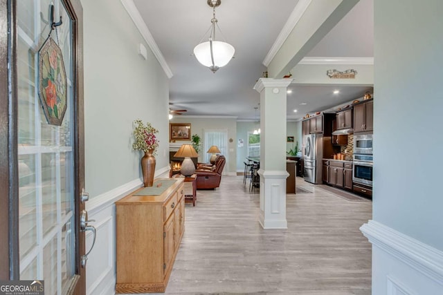foyer entrance featuring light wood-type flooring, a ceiling fan, crown molding, and decorative columns