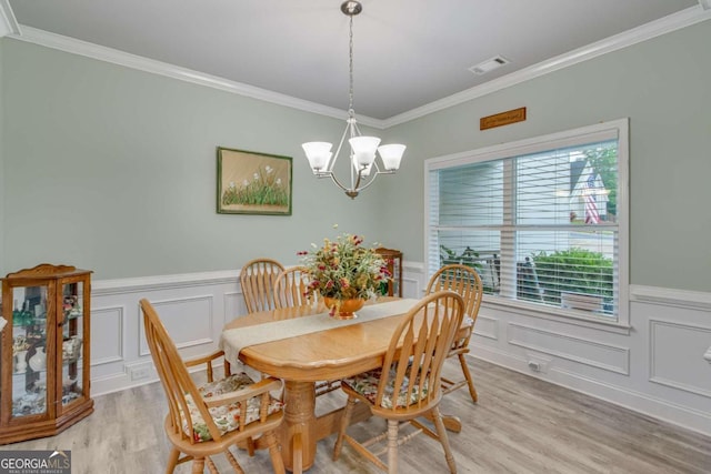 dining space featuring ornamental molding, a decorative wall, a chandelier, and light wood-type flooring