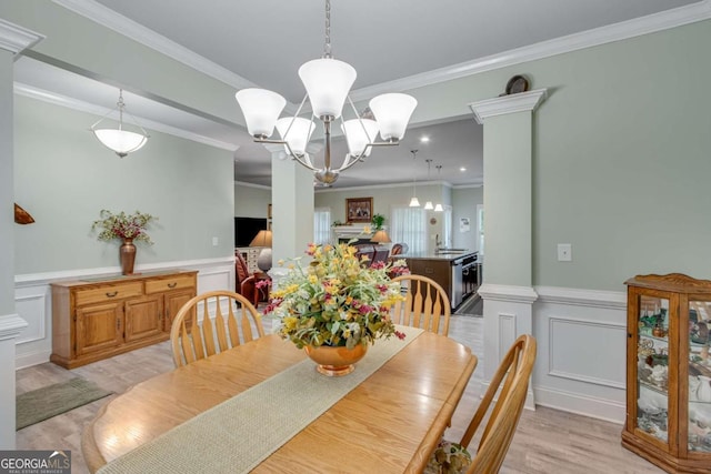dining space featuring a decorative wall, light wood finished floors, crown molding, a chandelier, and wainscoting