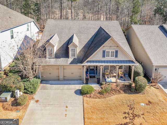 view of front of house featuring driveway, covered porch, an attached garage, a shingled roof, and stone siding