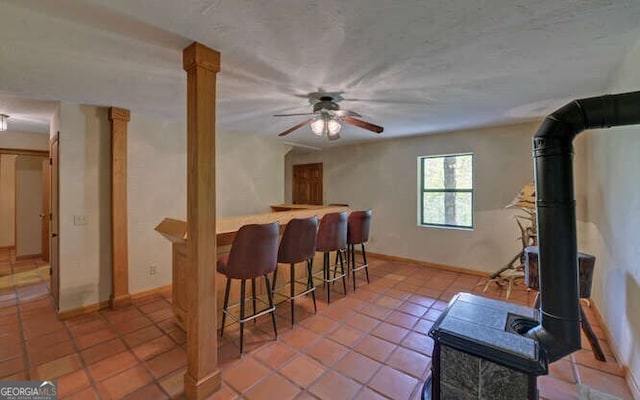 interior space featuring light tile patterned floors, a ceiling fan, bar, baseboards, and a wood stove