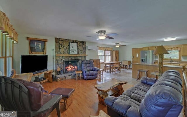 living area with light wood-type flooring, a stone fireplace, and a ceiling fan