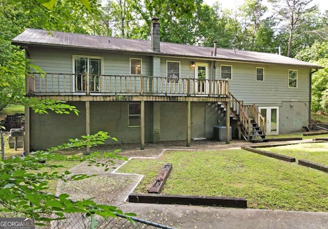 rear view of house with a chimney, a lawn, metal roof, a wooden deck, and stairs