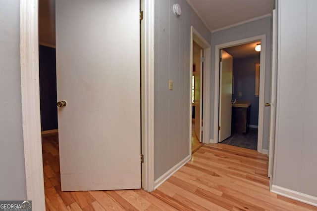 corridor with light wood finished floors, crown molding, and baseboards