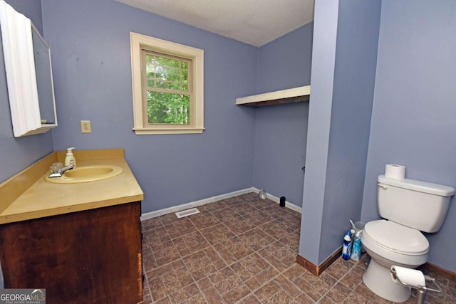 bathroom with baseboards, toilet, vanity, and visible vents