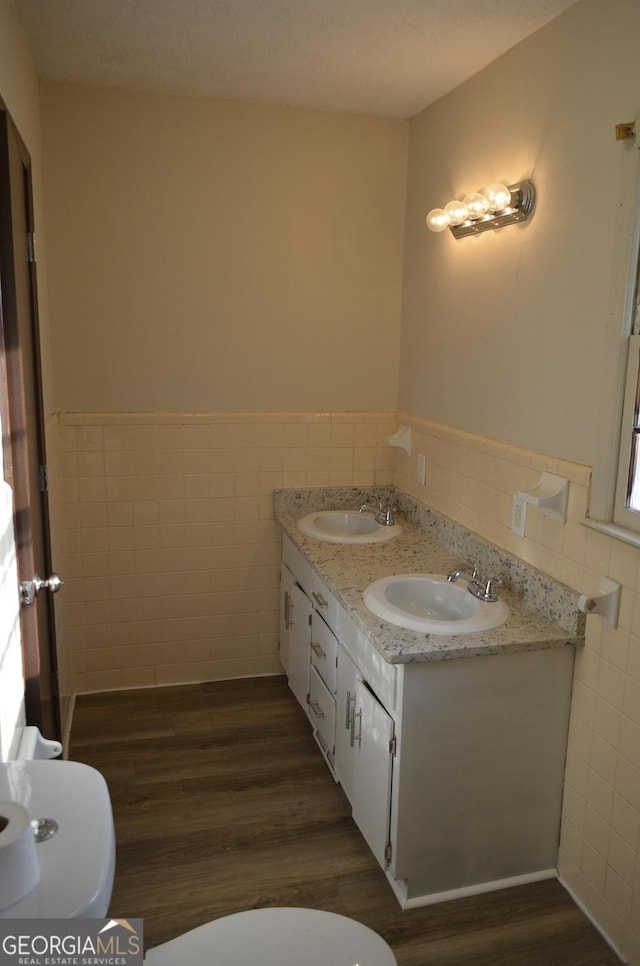 bathroom with toilet, tile walls, a sink, and wood finished floors