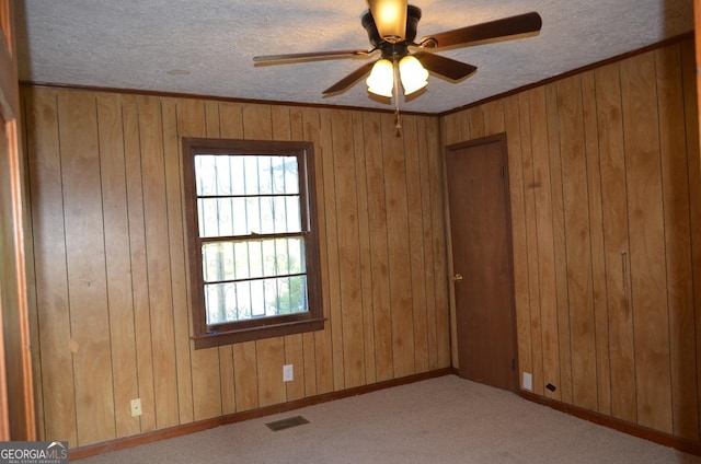 unfurnished room with wood walls, a textured ceiling, visible vents, carpet floors, and a ceiling fan