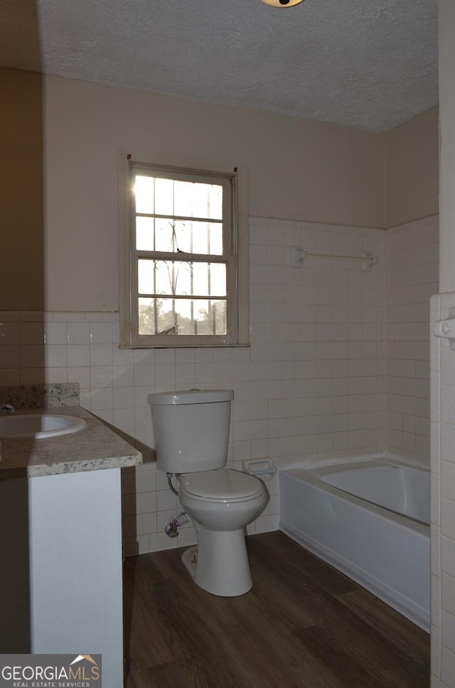 full bath with tile walls, toilet, wood finished floors, vanity, and a textured ceiling