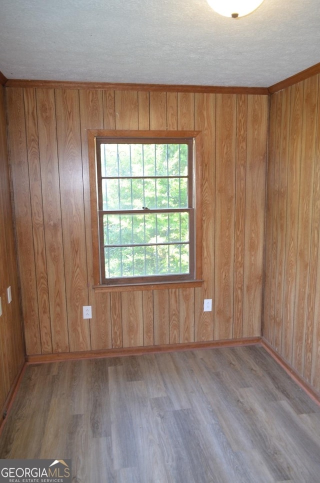 unfurnished room featuring wooden walls, a textured ceiling, baseboards, and wood finished floors