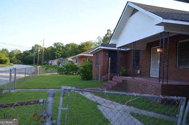 view of side of property featuring a porch, brick siding, a yard, fence private yard, and a shingled roof