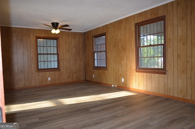 empty room featuring wood walls, wood finished floors, ornamental molding, a ceiling fan, and baseboards