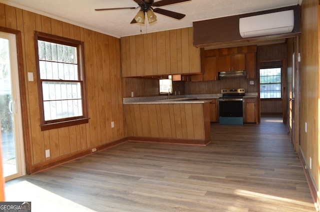 kitchen with a ceiling fan, a wall unit AC, under cabinet range hood, a peninsula, and electric range