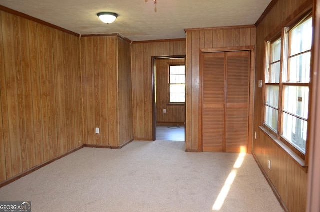 unfurnished room with light carpet, wooden walls, baseboards, and ornamental molding