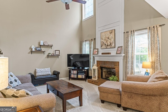 living area featuring a high ceiling, light carpet, a ceiling fan, and a brick fireplace