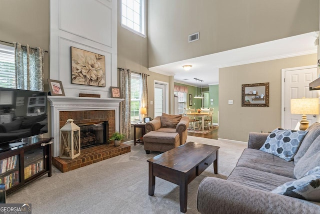 carpeted living area with baseboards, ornamental molding, visible vents, a towering ceiling, and a fireplace