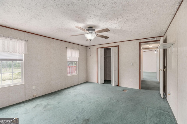 unfurnished bedroom with a textured ceiling, carpet flooring, a ceiling fan, and visible vents