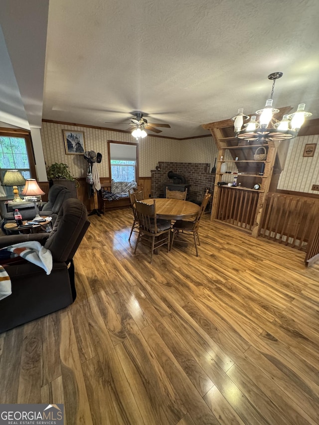 dining space with a textured ceiling, wood-type flooring, ceiling fan with notable chandelier, and wallpapered walls