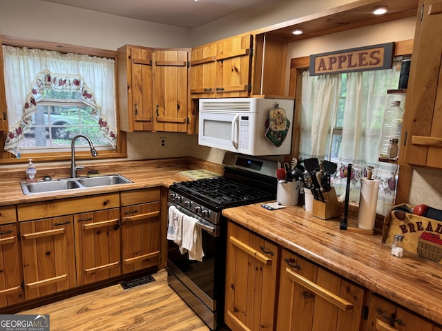 kitchen featuring stainless steel range with gas cooktop, white microwave, a sink, and plenty of natural light