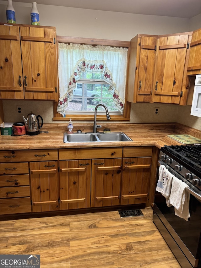 kitchen featuring a sink, white microwave, light wood-type flooring, light countertops, and stainless steel gas range