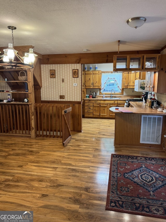 kitchen featuring light wood-style flooring, pendant lighting, brown cabinetry, a sink, and gas range