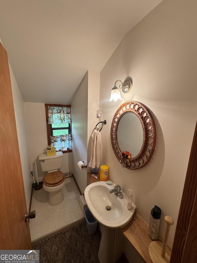 bathroom with toilet, vaulted ceiling, baseboards, and a sink