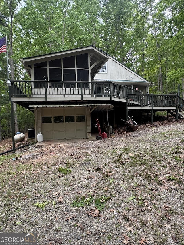 exterior space featuring an attached garage, a sunroom, dirt driveway, and a wooden deck