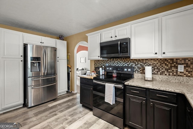 kitchen featuring arched walkways, white cabinetry, appliances with stainless steel finishes, and decorative backsplash