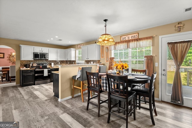 dining space with arched walkways, recessed lighting, light wood-style flooring, and visible vents