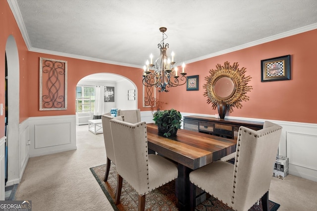 dining room featuring ornamental molding, wainscoting, a chandelier, arched walkways, and light carpet