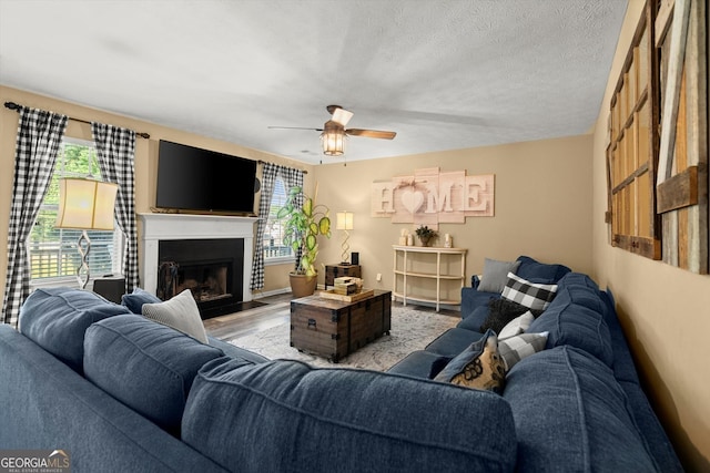 living area with a fireplace with flush hearth, a textured ceiling, wood finished floors, and ceiling fan