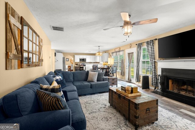 living room featuring a ceiling fan, a fireplace with flush hearth, light wood finished floors, and visible vents