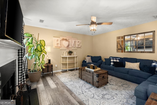 living area with a fireplace, a ceiling fan, visible vents, and wood finished floors