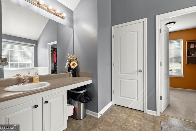 bathroom with baseboards, vanity, and vaulted ceiling
