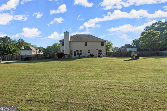 back of property with a fenced backyard, a chimney, and a lawn