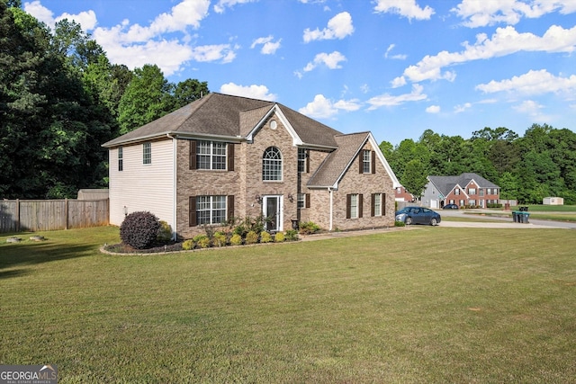 view of front of house with brick siding, roof with shingles, fence, and a front yard