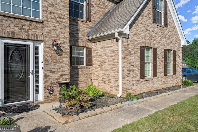 property entrance featuring a shingled roof and brick siding