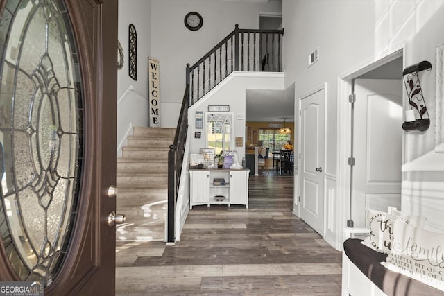 foyer featuring visible vents, dark wood-style flooring, a towering ceiling, and stairs