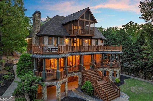4290 Bobbins Way, Cumming, GA 30041 - back of house at dusk featuring a balcony, stone siding, a chimney, and stairway
