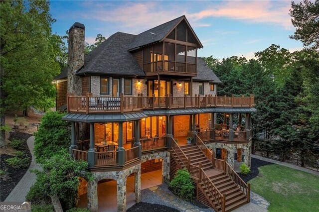 4290 Bobbins Way, Cumming, GA 30041 - back of house at dusk featuring a balcony, stone siding, a chimney, and stairs