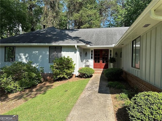 property entrance featuring french doors, a lawn, board and batten siding, brick siding, and roof with shingles