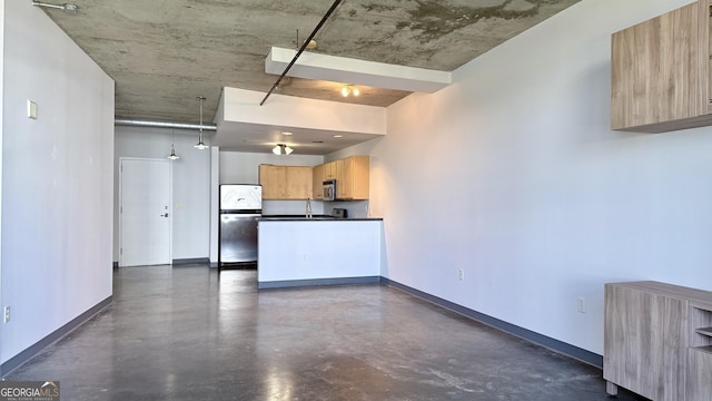 kitchen with a sink, light brown cabinetry, dark countertops, stainless steel appliances, and concrete flooring