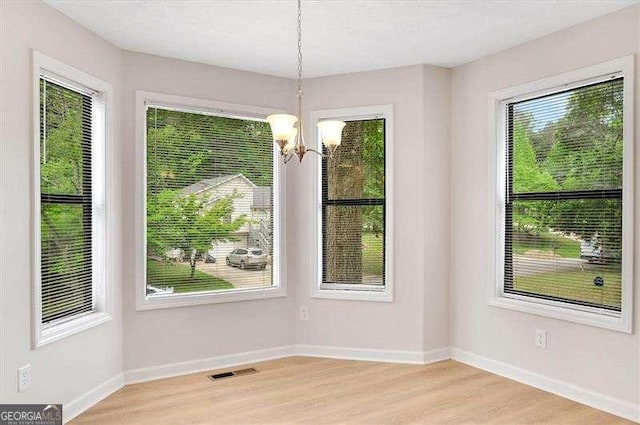 unfurnished dining area featuring an inviting chandelier, baseboards, light wood-type flooring, and visible vents