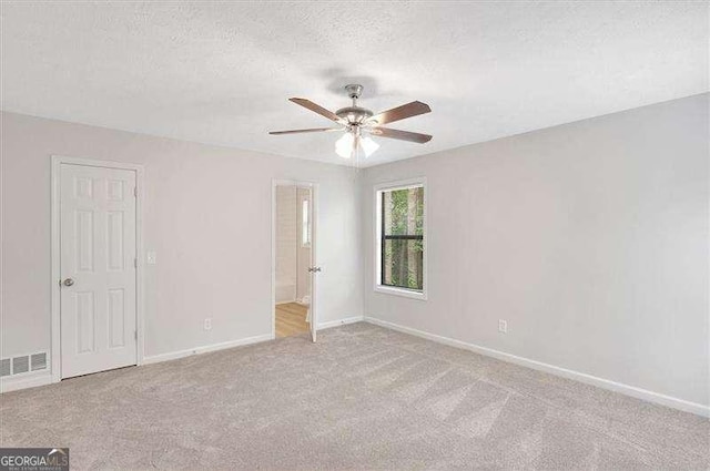 unfurnished room with a textured ceiling, carpet, baseboards, visible vents, and ceiling fan