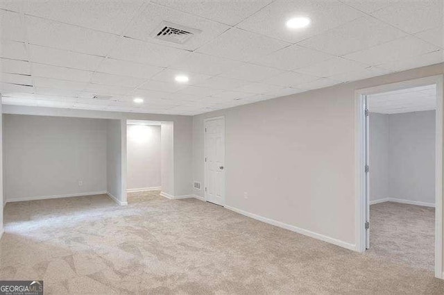 finished below grade area with a drop ceiling, visible vents, baseboards, light carpet, and recessed lighting