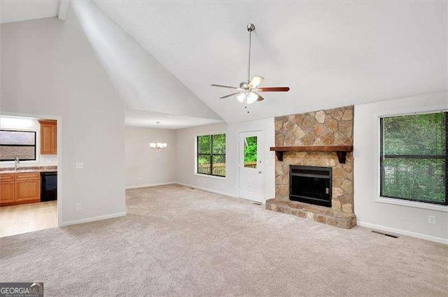 unfurnished living room with ceiling fan with notable chandelier, light colored carpet, high vaulted ceiling, baseboards, and a stone fireplace