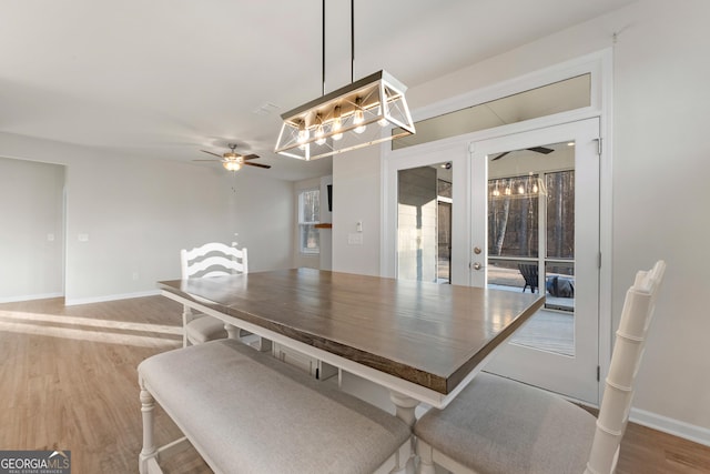dining area with baseboards, wood finished floors, and ceiling fan with notable chandelier