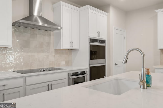 kitchen with a sink, wall chimney range hood, tasteful backsplash, black electric stovetop, and double oven