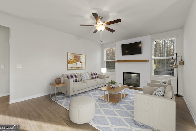 living room with wood finished floors, a healthy amount of sunlight, ceiling fan, baseboards, and a glass covered fireplace
